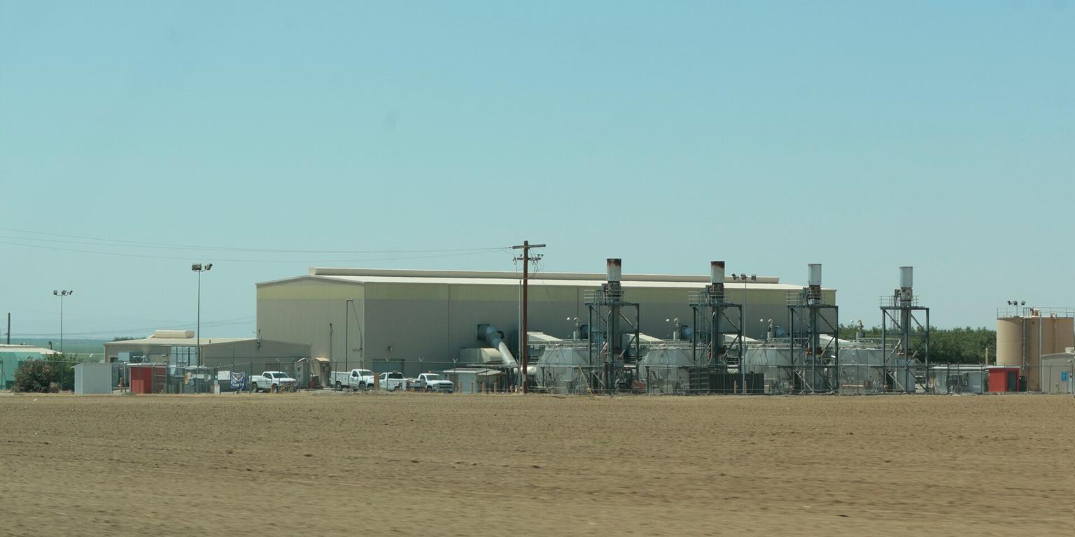 Gas compressor station with four exhaust stacks beside a plowed field at Wheeler Ridge, California