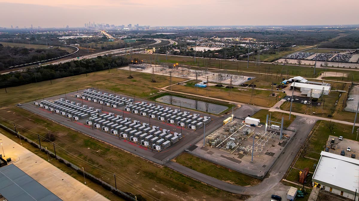 Aerial photograph of Jupiter Power's Callisto I battery storage site in central Houston, with rows of battery enclosures beside a substation and the downtown skyline on the horizon.