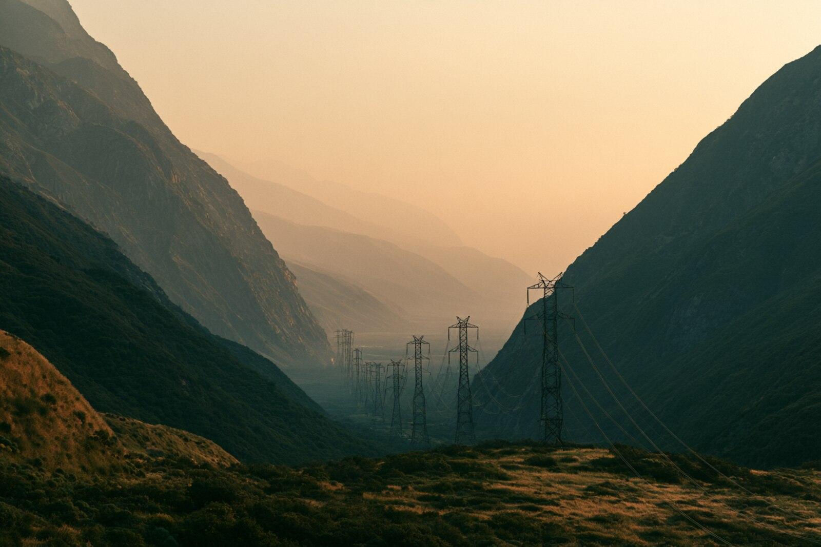 A single transmission line threading through a narrow mountain pass at golden hour
