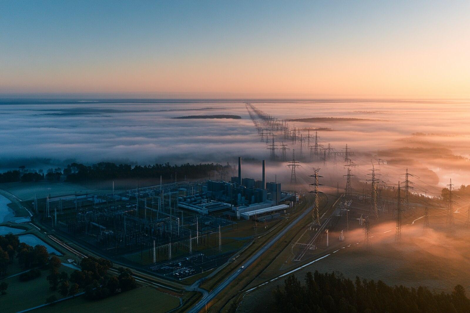 A power plant and switchyard photographed at sunrise, morning fog giving way to open sky
