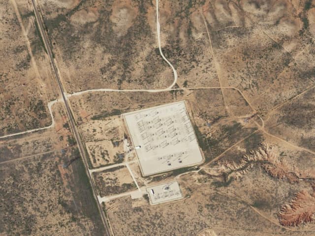 Aerial view of the Borden County battery storage site: a rectangular gravel pad filled with rows of battery containers beside an electrical substation, surrounded by scrubland.